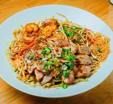 Hu tieu noodles with sliced pork and shrimp, bean sprouts and herbs, served on a white plate