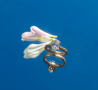 Gold diamond ring styled with pale flower petals on a blue background