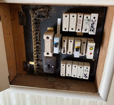 Old electrical switchboard with ceramic fuses and circuit breakers in a recessed wall niche.