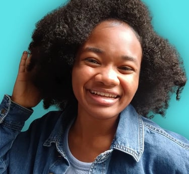 A smiling Black woman with voluminous natural hair wearing a denim jacket against a bright teal background.