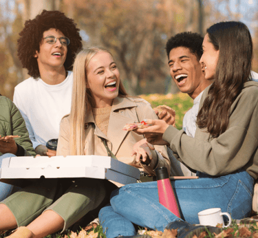 Diverse group of smiling friends enjoying a pizza picnic outdoors in a sunny autumn park.