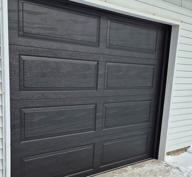 Modern black raised panel sectional garage door installed on a residential home with white siding.