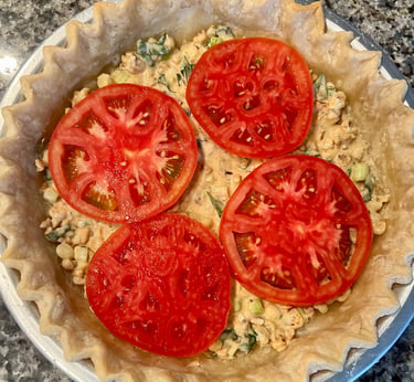 Freshly sliced red tomatoes layered on top of a savory pie filling in a fluted pastry crust.