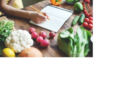 Photo of a person writing in a journal on a table that also has colorful ingredients on it