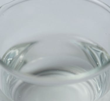 Close-up macro shot of liquid viscosity in a glass beaker, showing subtle texture and light refraction, clean neutral studio lighting, cool desaturated tones, sharp focus, shallow depth of field, clinical aesthetic