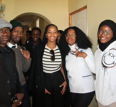 A group of diverse, smiling young African students posing together in a brightly lit hallway.