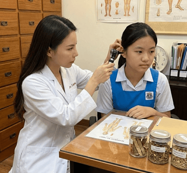 A Chinese TCM physician is doing and ear check on a teenage girl.