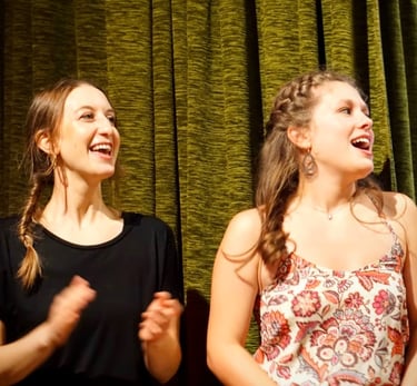 zwei junge Frauen auf der Bühne, die mit Freude singen