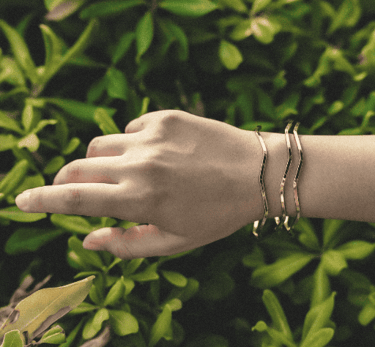 Elegantes brazaletes de oro con diseño ondulado, lucidos en una muñeca sobre un fondo de naturaleza