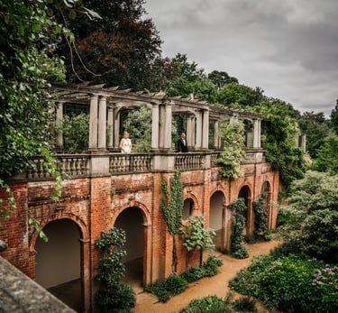 Bride and groom standing on a terrace of a historic brick building surrounded by greenery
