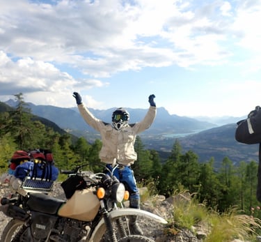 a man standing on a mountain top with his arms up in the air