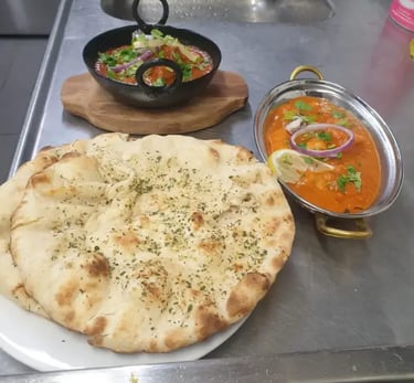 Authentic Indian butter chicken and lamb curry served with fresh garlic naan bread on a metal kitchen counter.