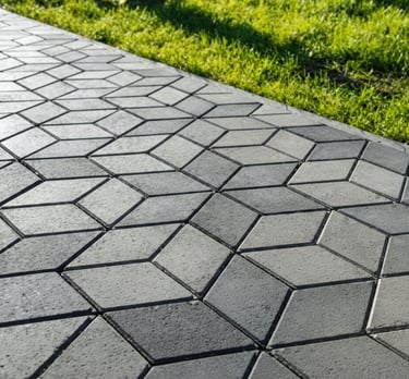 Gray 3D geometric interlocking paving stones installed along a vibrant green grass lawn edge.