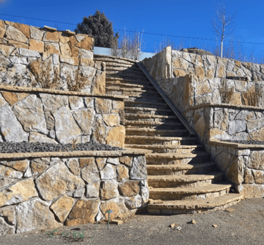 Multi-level natural stone retaining walls and matching stone stairs in a terraced backyard landscape.