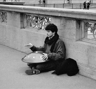 a man sitting on the sidewalk playing the handpan instrument.
