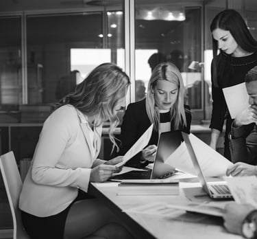 a group of people sitting around a table looking intently at paperwork and screens