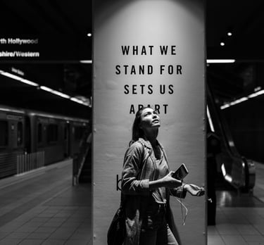 grayscale photo a woman standing in a subway station next to a social impact ad