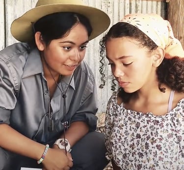 a young woman in a sheriff hat speaking to and a teen girl in a head scarf