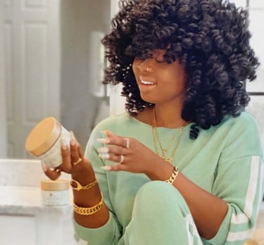 black woman with afro looking at a jar of ori by flametree shea butter
