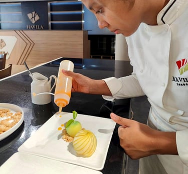 a chef in a white uniform is pouring a sauce on a plate
