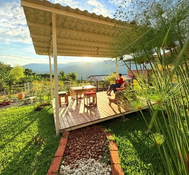 Mujer sentada en una terraza de madera con una mesa y sillas disfrutando del atardecer