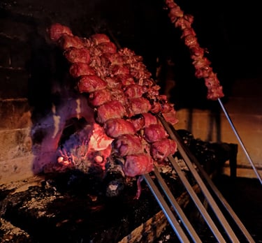 Traditional Italian meat skewers grilling over a rustic wood-fired brick oven with glowing embers.