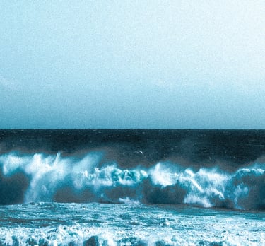 Dramatic blue ocean waves crashing onto a sandy beach under a clear sky.