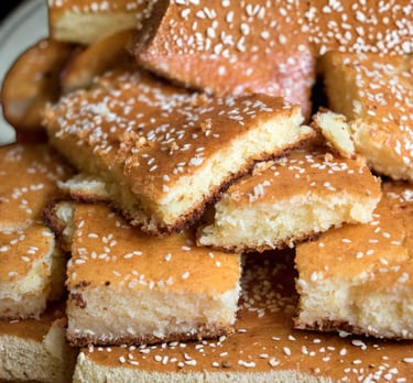 Slices of golden-brown semolina cake topped with white sesame seeds, a classic Middle Eastern dessert.