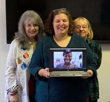 a woman holding a laptop computer and smiling with two more women behind her
