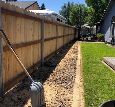 a grassy lawn with cleared area and shovel propped up against fence