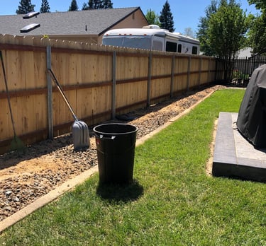 a grassy backyard with cleared area and trash can near fence line 