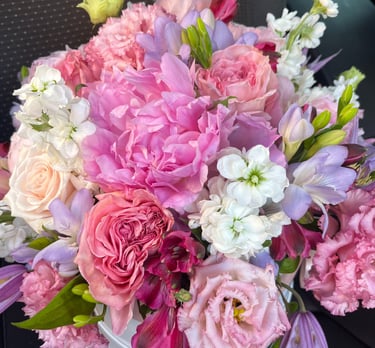 A vibrant pink and purple floral arrangement featuring peonies, roses, and white stock flowers.