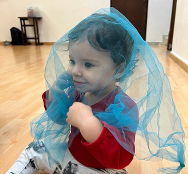 Niña sentada en piso de madera cubierta por una malla azul transparente en Ukelele Jardín Infantil