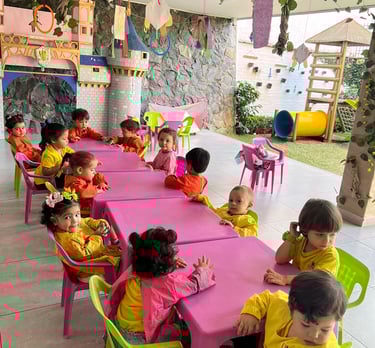 Niños sentados en mesas rosadas con sillas verdes en Jardín Infantil Ukelele
