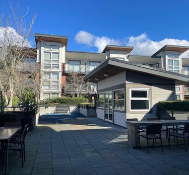 Modern apartment building rooftop patio with outdoor dining tables and a grey clubhouse.