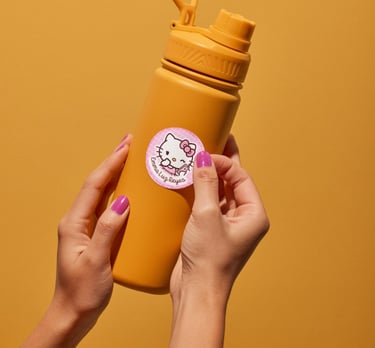 Hand applying a custom Hello Kitty sticker label to a yellow reusable water bottle.