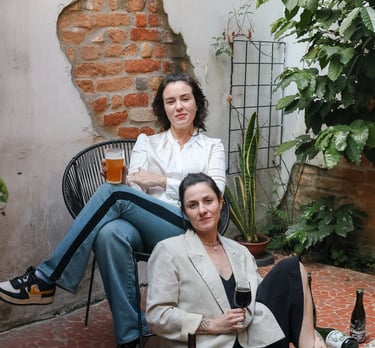 Two women enjoying craft beer and wine in a rustic outdoor patio with exposed brick.