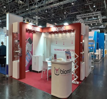 Bespoke red architectural exhibition pavilion for Biomat at Medica Düsseldorf featuring integrated glass showcases.