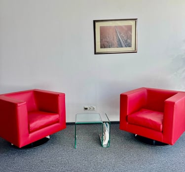 Two modern red leather swivel armchairs in a minimalist office waiting area with a glass side table.