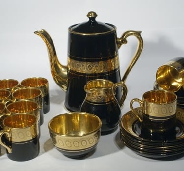 Vintage black and gold porcelain coffee set including a tall pot, creamer, sugar bowl, cups, and saucers.