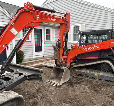 Orange Kubota SVL75-3 skid steer and excavator performing residential excavation and landscaping.