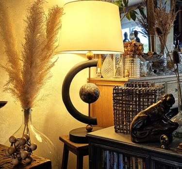 Modern black table lamp with warm lighting on a wooden stand surrounded by boho home decor and dried pampas grass.
