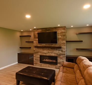 A basement living room in Minnesota with floating wood shelves, a fireplace and a stone wall. 
