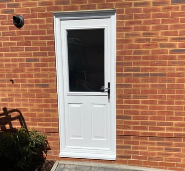 a white composite back door with chrome handle and half glazing on a red brick house.  It was fitted by buildmydoor