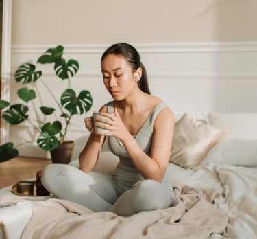 a woman sitting on a bed with a cup of coffee