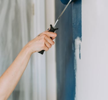 a woman is painting a wall with a blue paint roller