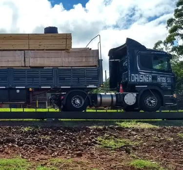 A black Drisner Hnos flatbed semi truck transporting stacks of lumber.