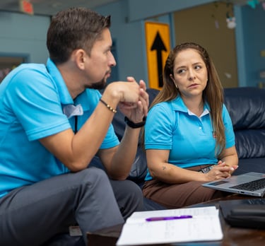 Two colleagues in blue polo shirts discuss project data over a laptop in a modern office lounge.