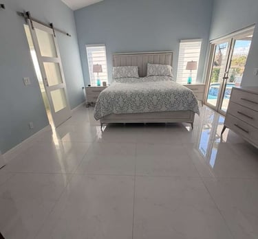 Elegant light blue bedroom with a white bed, tall ceilings, large windows, and sleek white tile flooring, perfect for a