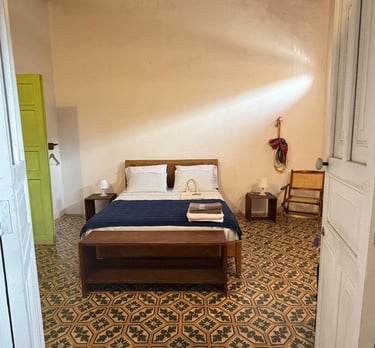 Rustic hotel room with vintage patterned tile flooring, a wooden bed with blue linens, and a bright lime green door.